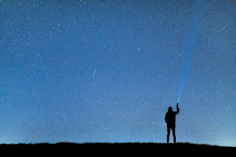 A person with a flashlight gazing at the stars, creating a silhouette against the night sky.