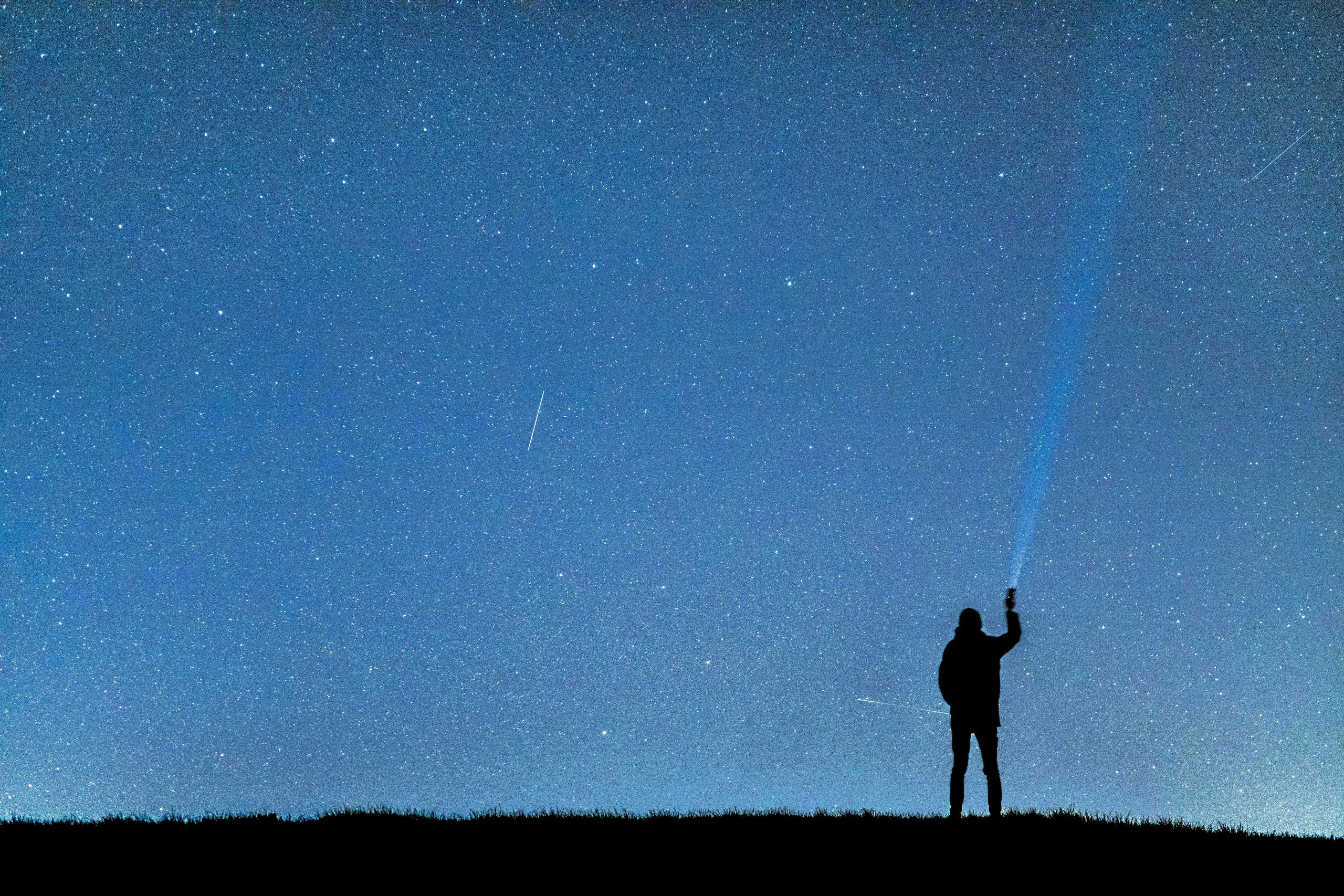 A person with a flashlight gazing at the stars, creating a silhouette against the night sky.