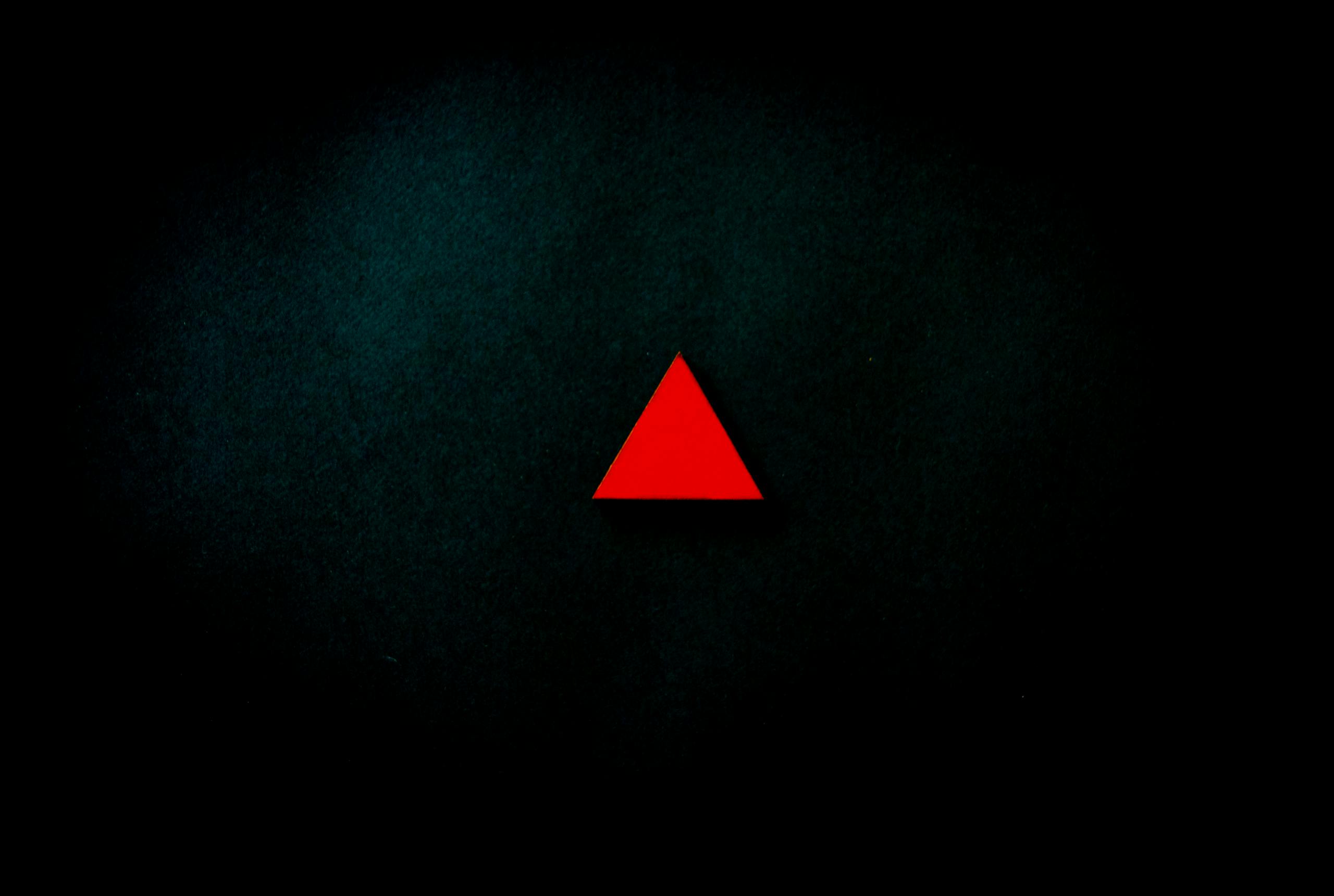 A striking minimalist image of a red triangle centered on a dark, textured background.
