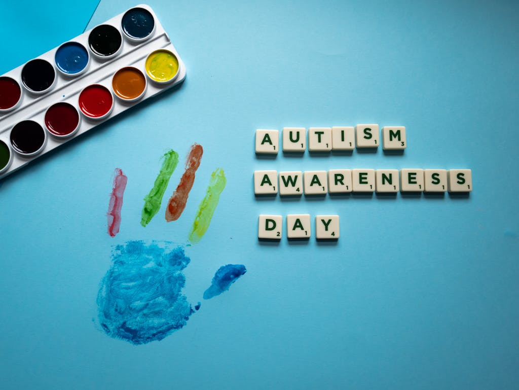Colorful autism awareness composition with watercolor set and scrabble tiles emphasizing creativity and support on blue background.