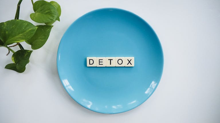 Minimalist concept of detox with letter tiles on a turquoise plate and green leaves.